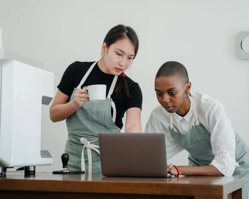 An experienced barista showing a new team member the café system